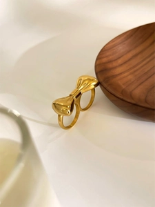 Bague double doigt dorée polie avec un nœud papillon 3D sur un plateau en bois
