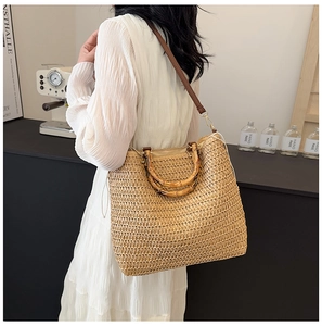 Detail of woven straw tote bag featuring vintage bamboo handles and brown leather strap