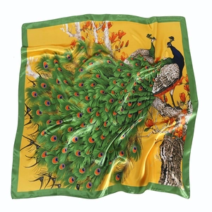 Detailed pattern of peacocks and flowers on a glossy yellow silk scarf with green edges