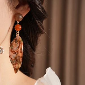 Close-up of tortoise shell leaf drop earrings with brown beads and golden metal finish