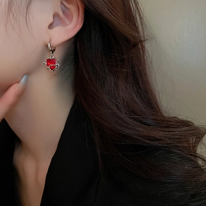 Detail of red heart zircon earring with silver thorn design worn on female ear