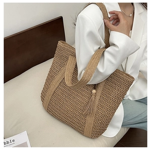 Detail of khaki straw tote bag featuring thick woven texture and tassel pendant accessory