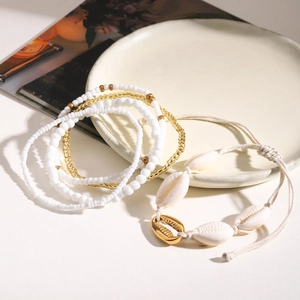 Flat lay of bohemian anklet set with white beads, natural shells and gold accents