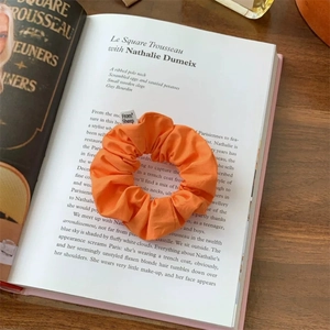 Detailed view of an orange pleated fabric scrunchie on a book with a From Sheep label
