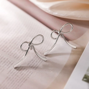 Boucles d'oreilles nœud argentées posées sur un livre ouvert avec une lumière vintage