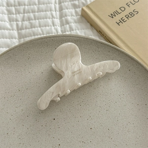 Detail view of large marble texture acetate hair claw clip on a minimalist display