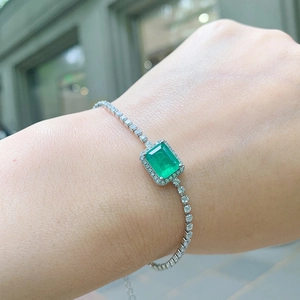 Close-up of emerald-cut green gemstone bracelet on wrist with silver diamond-set chain