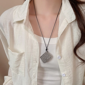 Detail of silver mesh square pendant on black cord necklace worn with white shirt
