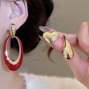 Detail view of heart-shaped gold studs and red enamel earrings on a model