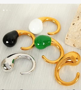 Detail of drop-shaped C-style earrings in gold, silver, black, white, and green enamel finishes