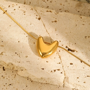 Close-up of a polished gold heart pendant with a fine snake chain on beige stone