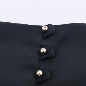 Détail du tissu noir d'une robe ballon avec trois boutons sphériques dorés polis