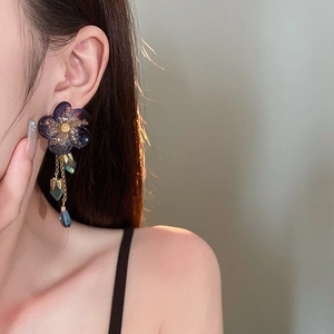 Close-up of blue flower earrings with gold metal tassels and crystal pendants on model