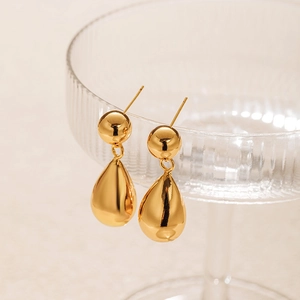 Elegant gold drop earrings with polished sphere and teardrop pendants on glass