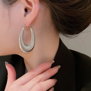 Close-up of polished silver oval hoop earrings with spiral ribbed texture on model
