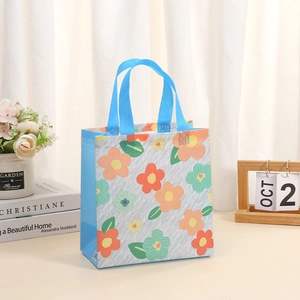 Graue Vlies-Einkaufstasche mit blauen Henkeln und Blumenmuster auf hellem Schreibtisch