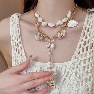 Detail of layered gold necklace featuring natural seashells, starfish, and pearls on white lace