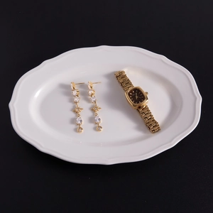 Detail of gold tassel earrings with star zircon and vintage square watch on a plate