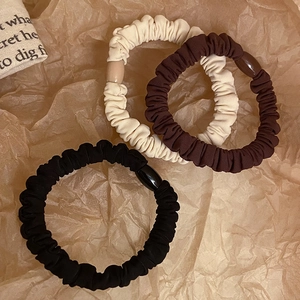 Three premium knit scrunchies in cream, coffee, and black on vintage textured paper