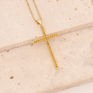 Detailed view of a gold cross pendant necklace featuring amber zircon stones on stone