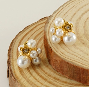 Close-up of golden flower earrings with white pearls and diamonds on wooden stand