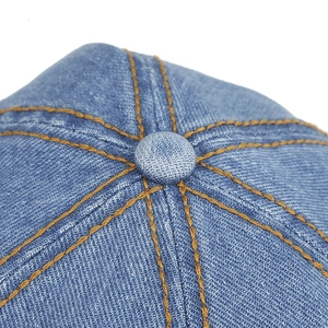 Makro-Detailansicht einer blauen Denim-Mütze mit gelben Nähten und stoffbezogenem Knopf