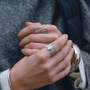 Close-up of adjustable silver-tone liquid lava rings and a wide cuff on a wool coat sleeve