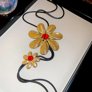 Detail of flower sweater necklace with gold brushed petals and red gemstone center