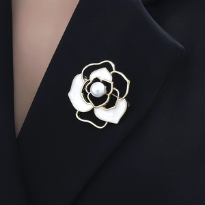 Elegant gold camellia flower brooch with white enamel petals and pearl center on black suit