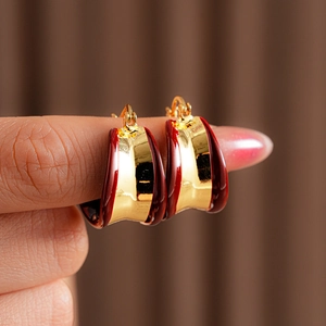 Détail de boucles d'oreilles dorées en U avec émail rouge entre les doigts