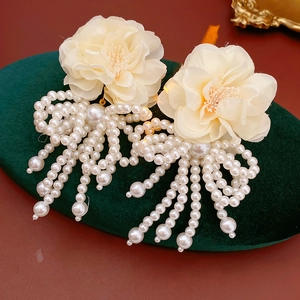 Detailed close-up of cream fabric flower earrings with white pearl tassels on velvet