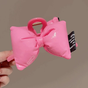 Close-up of a pink puffy bow hair claw clip with a black fabric logo label for girls