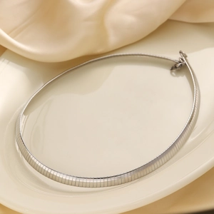 Close-up of polished silver flat snake chain necklace on a minimalist silk background