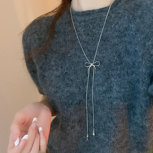 Silver bow pendant necklace on a dark grey sweater showing elegant fashion styling