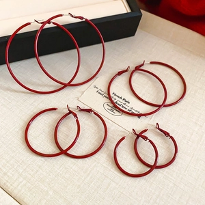 Close-up of four pairs of graduated red hoop earrings on a minimalist display