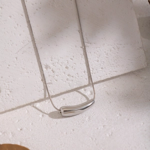 Macro shot of minimalist silver arc pendant and sleek snake chain on white stone
