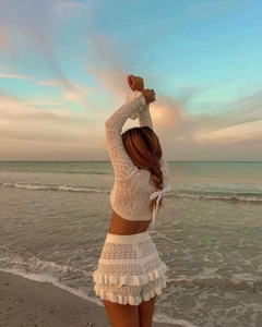 Detail of white knitted crop top with back bow tie and hollow out patterns on beach