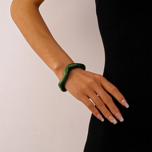 Detail of a wavy green acrylic cuff bracelet worn on a wrist against a black sleeve