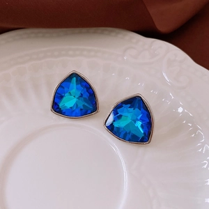Macro shot of blue triangle gemstone earrings with silver-tone base on a ceramic plate