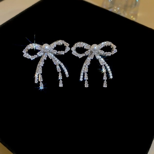 Macro shot of silver bow earrings with pave crystals and hanging tassel on black velvet