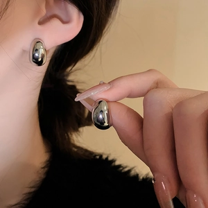 Close-up of a polished silver C-shaped bean stud earring on ear showing glossy finish