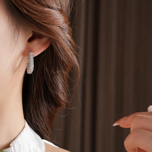 Gros plan de petites créoles carrées en argent avec zircons sur l'oreille