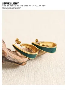 Detailed close-up of C-shaped gold-plated steel earrings with green enamel on dark wood