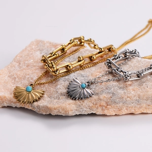 Close-up of gold and silver layered necklaces with fan pendants and turquoise beads