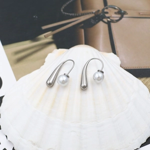 Detailed close-up of water-drop silver earrings and pearl resting on a white seashell