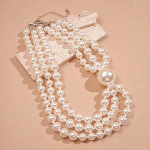Three-layer faux pearl necklace with large accent bead on textured stone background