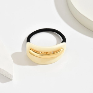 Detailed shot of acetate hair tie with golden metal inlay on a creamy white base