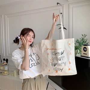 Detail of artistic letter print on a cream canvas tote bag held by a model