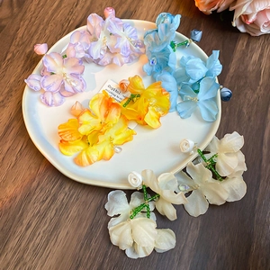 Flat lay detail of floral drop earrings in purple, blue, yellow, and white on wood