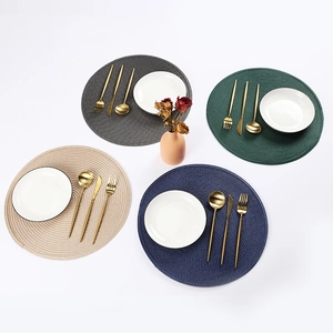 Close-up of four-piece woven round placemats with plates and cutlery in minimalist home setting